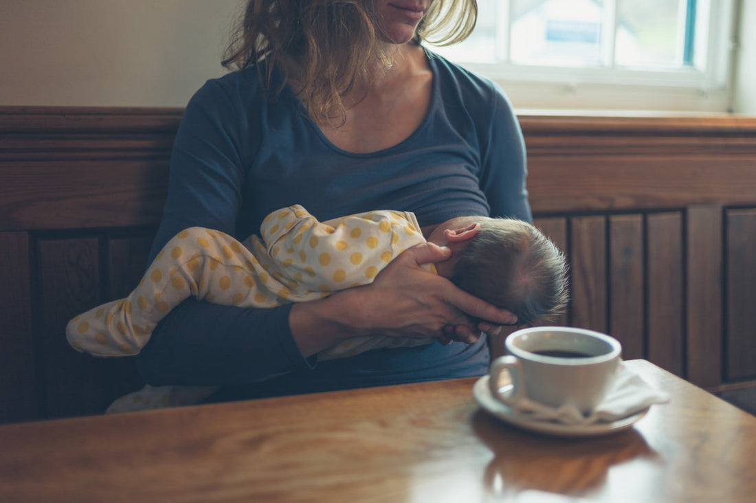 Mother nursing her baby at a table beside a cup of coffee