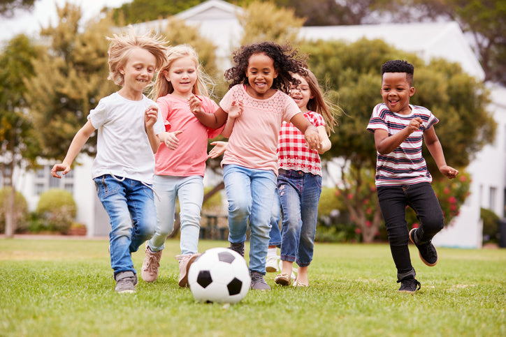 Group of kids running after a soccer ball on a backyard lawn