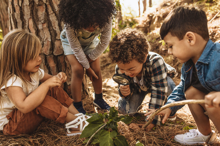 Young kids exploring the forest floor with a magnifying glass