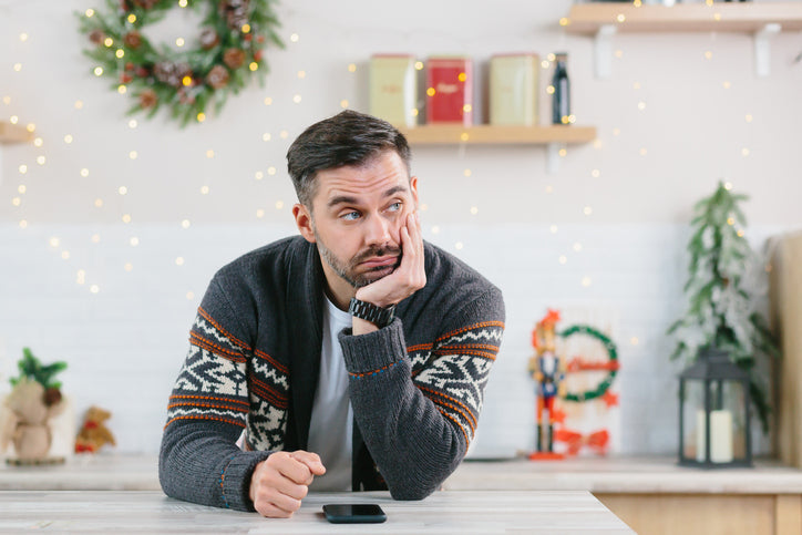 Man in a winter sweater resting his chin on his hand in a festive kitchen