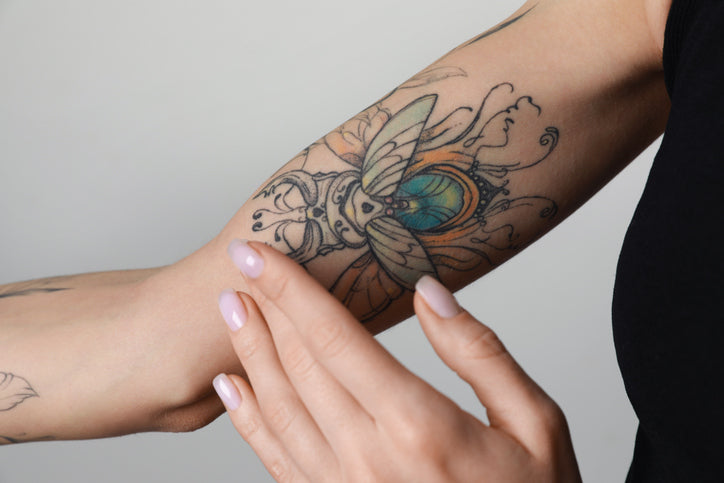 Close-up of a hand touching a colorful beetle tattoo on a forearm