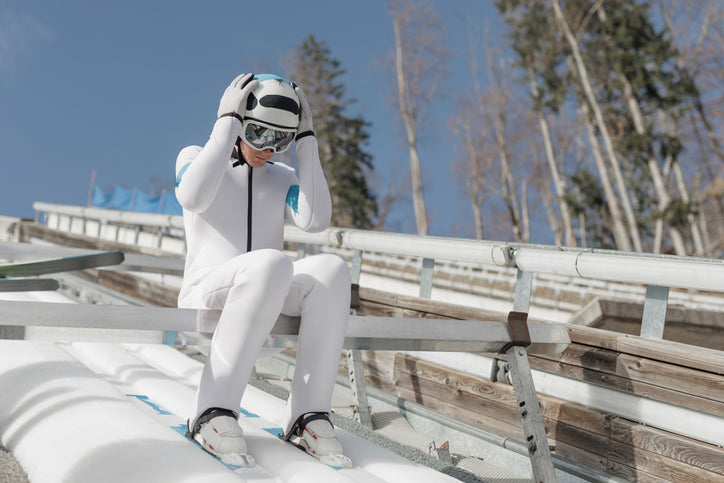 Ski jumper in white gear sitting at the top of a ski jump