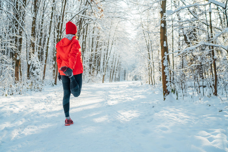 Runner in a red jacket stretching on a snowy forest path